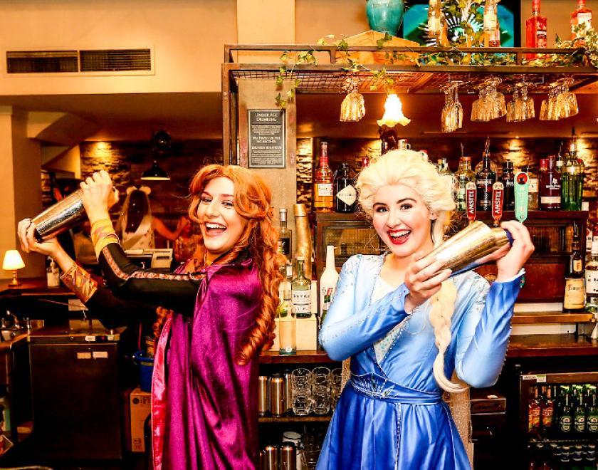 women dressed as Anna and Elsa shaking cocktails in a bar