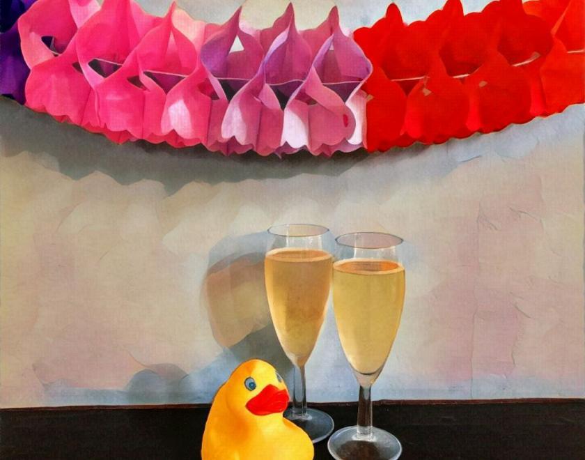 A yellow rubber duck guards two full champagne flutes under a pink, lilac  and red paper decorative garland