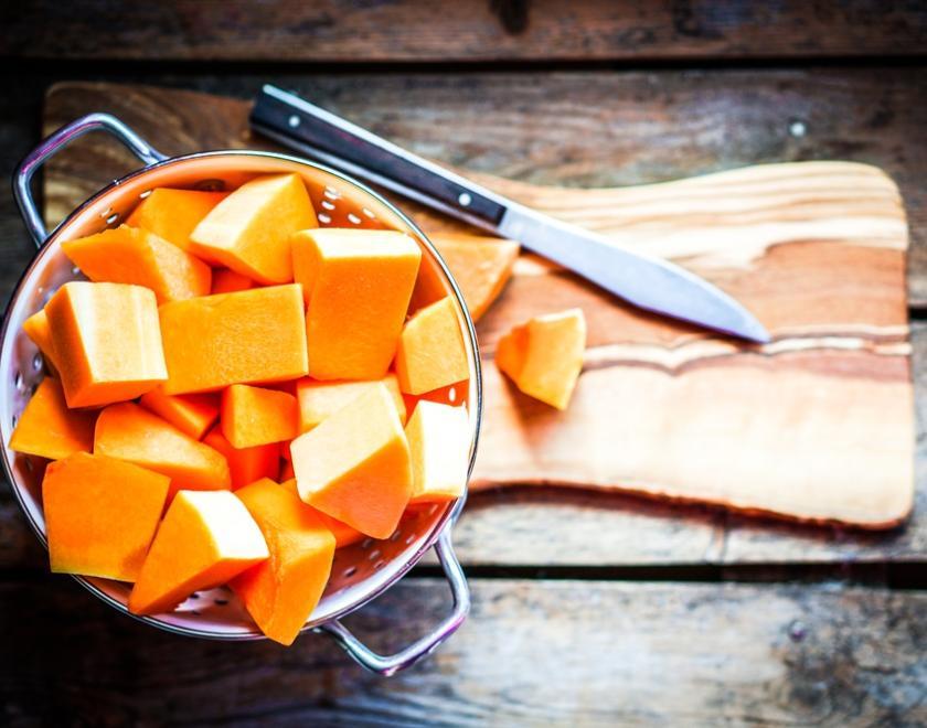 Chopped pumpkin in a sieve on chopping board with a knife lying next to it.