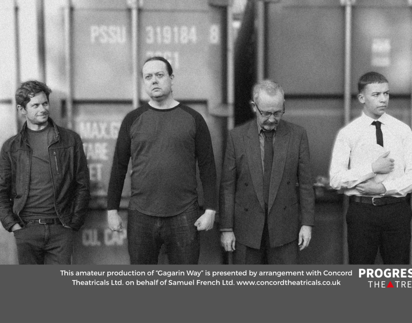 Grainy black and white image of four men standing a row with details of the production at the bottom
