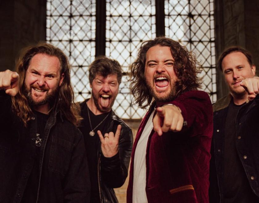 Four members of the band making a screaming expression and pointing at the camera