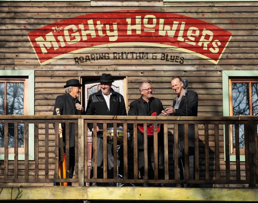 The Mighty Howlers band members standing outside a wooden shack