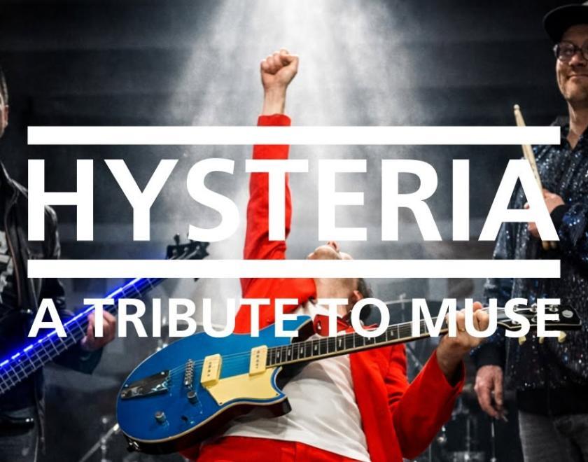 Three band members standing around - the lead guitarist in the middle is leaning back with his fist in the air