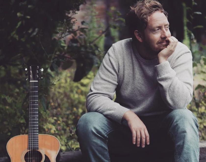 photo of singer James Krby in a grey jumper next to his guitar at Village Concerts in Purley-On-Thames