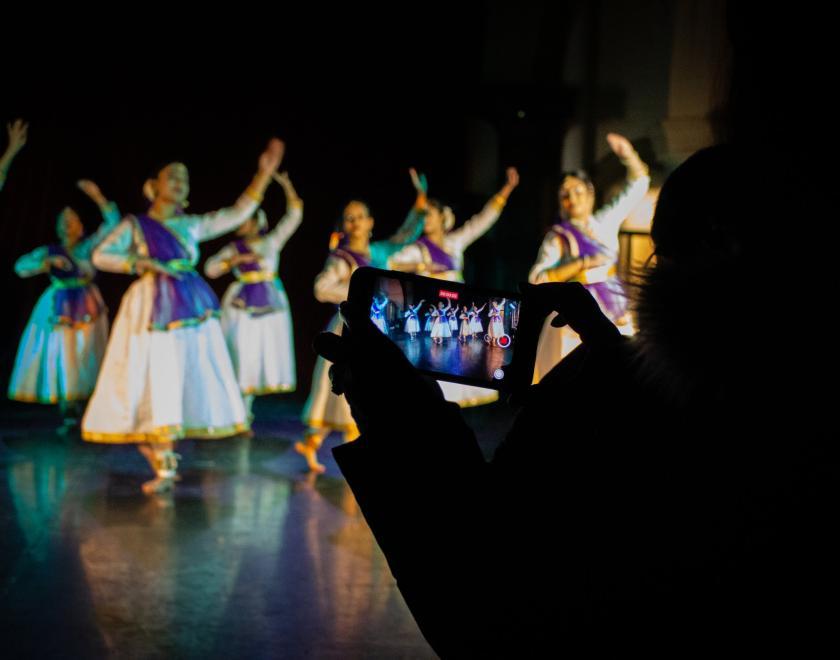 South Asian dancers on a stage with a mobile phone taking a photo of them