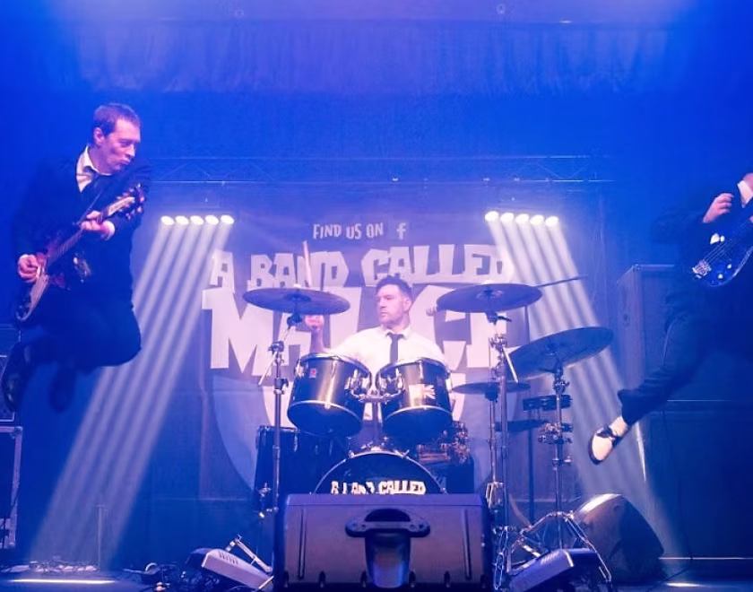 A Band Called Malice on stage. The guitarist and bass player are jumping into the air with their instruments.