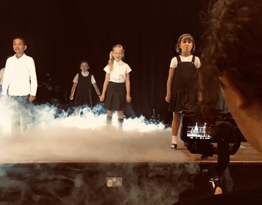 Children on stage with dry ice, being filmed by a digital camera