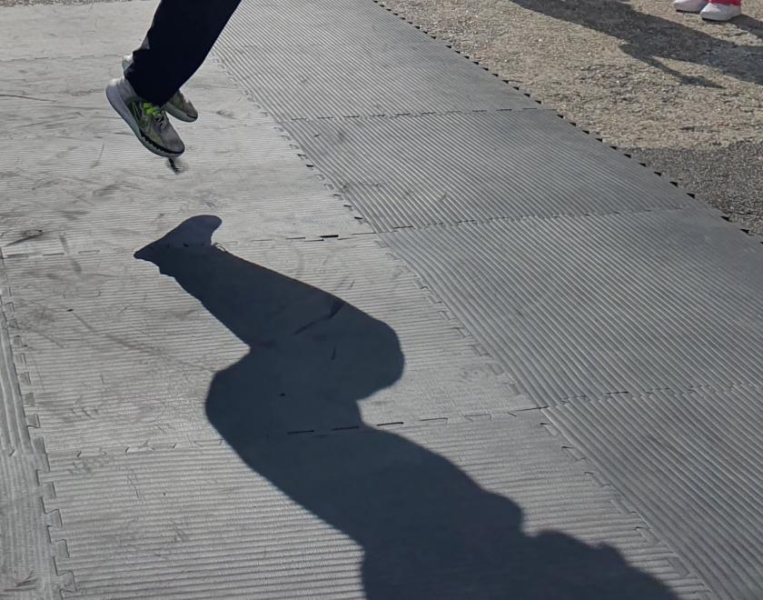  photo of a dancer jumping the air with only their feet and full shadow on the floor visible.