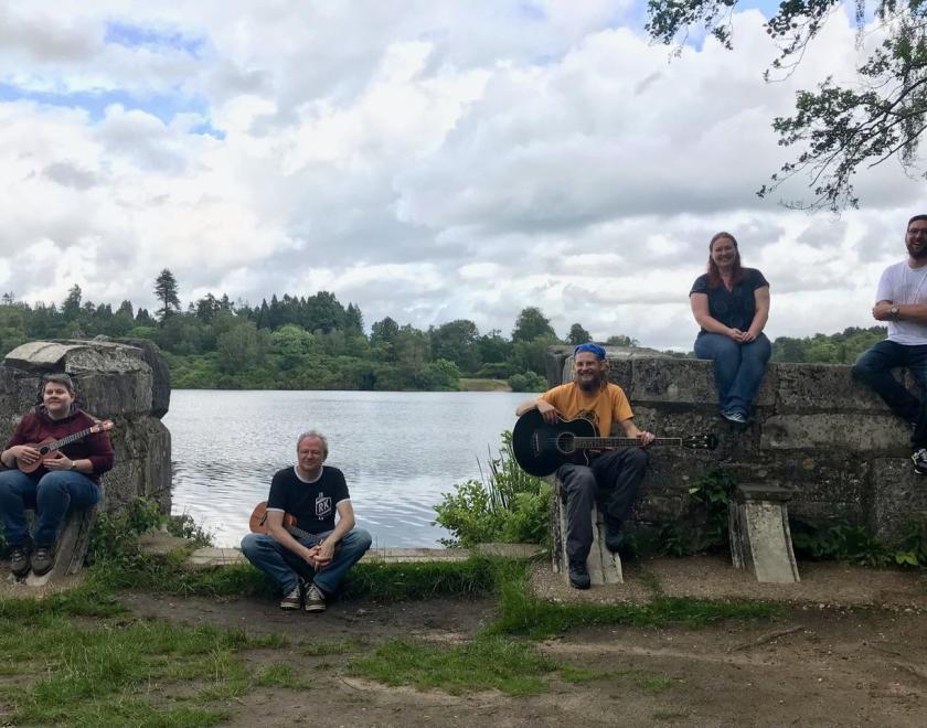 Miscellaneous musicians with their instruments sitting on some old walls by a large body of water