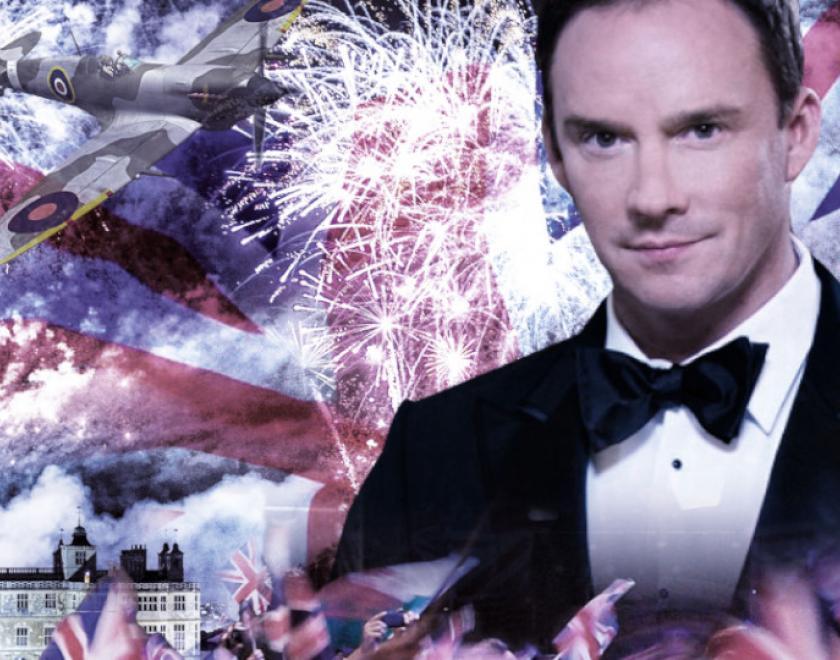 Russell Watson in a tuxedo surrounded by Union Jacks and fireworks