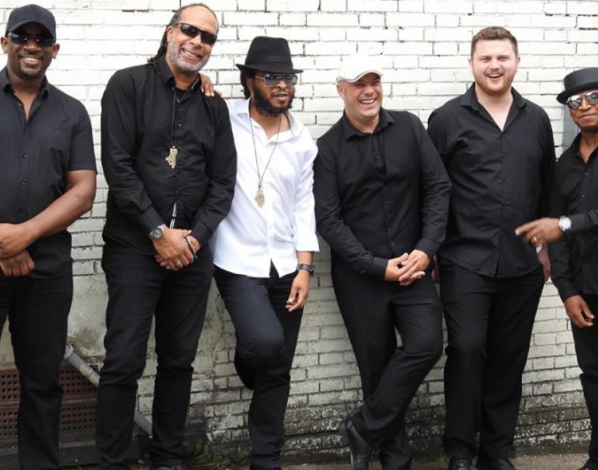 Members of Strictly UB40 wearing black lined up against a white brick wall