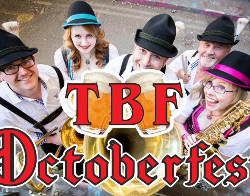 Image of a band dressed in Bavarian costumes and holding instruments with the TBF Octoberfest logo over the top