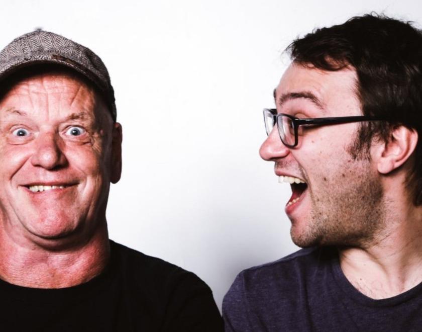 Two middle-aged men - one in a cap, gurning at the camera, the other in glasses with a shocked grin