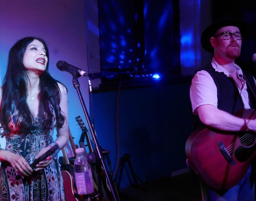 Tomorrow Bird on stage - a woman with long dark hair singing, and a man with glasses and a ginger beard playing guitar