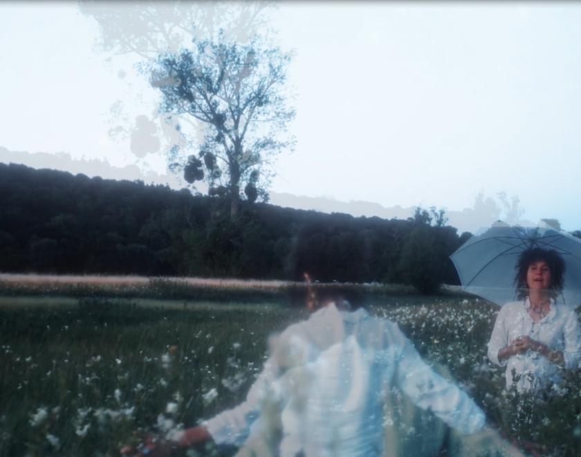 Video still featuring several superimposed images of a curly-haried woman in a field
