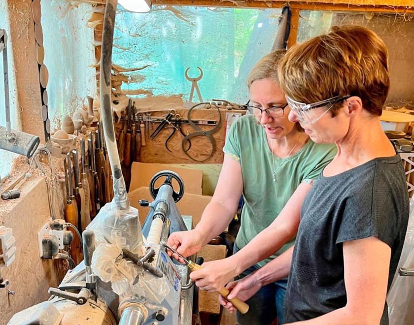Woman learning how to woodturn at a lathe with Liz Pearson.