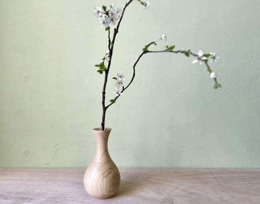 A wooden bud vase containing a sprig of cherry blossom.
