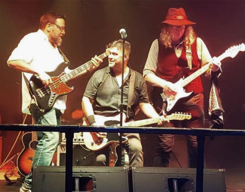 three men playing guitars on stage