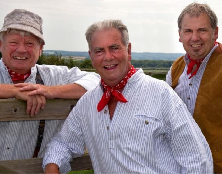 The Wurzels wearing country clothes and standing by a fence