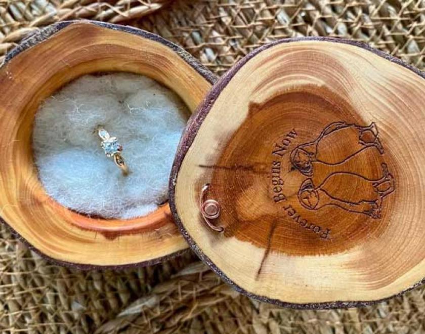 Yew ring box with white felted insert and engraved lid holding an engagement ring.